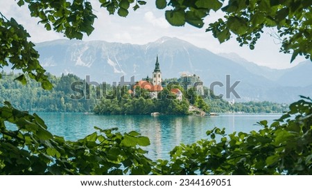 Beautiful picture of Bled Lake with green leaves making a frame and with blue tones on the water on a sunny day	