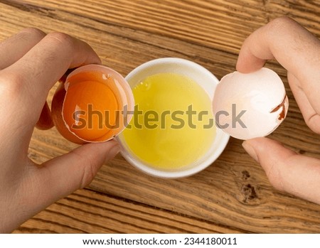 Broken Egg in Hand, Raw Yolk and White Separation, Cracked Brown Shell, Fresh Broken Organic Chicken Eggs on Wooden Rustic Background Royalty-Free Stock Photo #2344180011