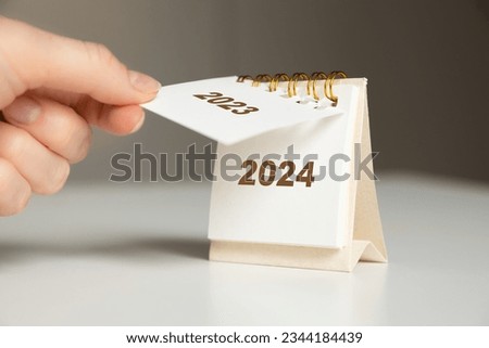 a woman's hand turns over a calendar sheet. year change from 2023 to 2024 Royalty-Free Stock Photo #2344184439