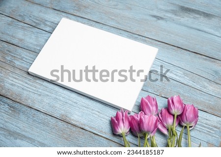 Blank white canvas mockup with flowers on blue wood background. Rectangular canvas, blue wood backdrop