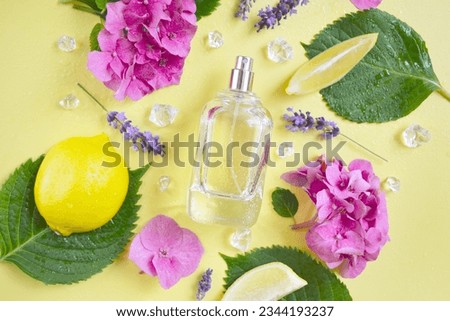 Glass transparent bottle of perfume with  lemons, hydrangea, lavender flowers, green leaves, ice cube, water drops and  on the yellow background. Fresh summer unisex smell. Hot summer scent. Royalty-Free Stock Photo #2344193237