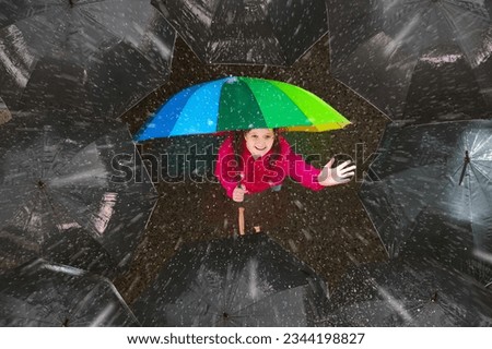 Happy young girl under colorful umbrella in dark crowd in autumn rain. Happiness and optimism concept. Joy and hope in difficult situations. Problem solving and creativity. Stand out and be unique. Royalty-Free Stock Photo #2344198827
