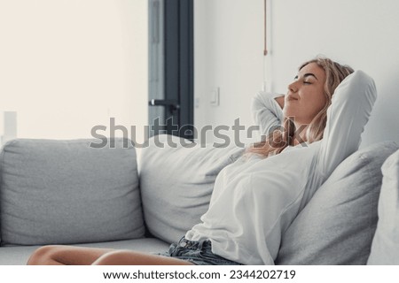 Young calm woman chilling relaxing leaning on comfortable sofa napping on couch in living room resting having healthy quiet nap, breathing fresh air, no stress free weekend at home, peace of mind Royalty-Free Stock Photo #2344202719