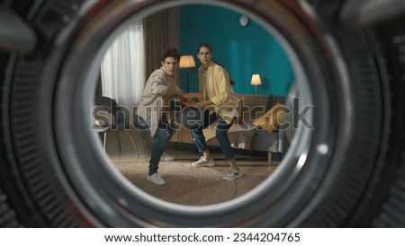 View from inside the empty washing machine young couple with laundry basket throwing clothes inside the washer Royalty-Free Stock Photo #2344204765