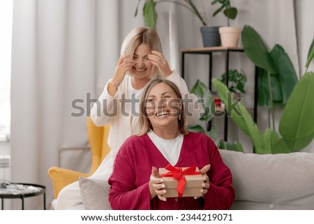 Lifestyle Adult daughter gives gift to happy elderly parent mother in living room. Concept family day of mom.