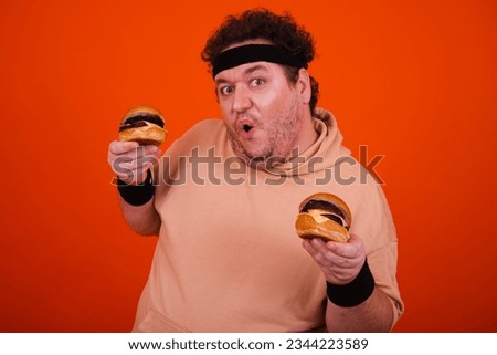 Funny fat man in the gym doing fitness and eating burgers.