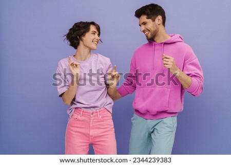 Young smiling couple wearing pastel clothes dancing isolated over purple studio background