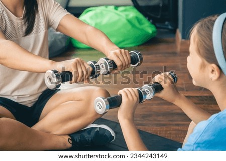 A woman with the daughter doing sports with dumbbells at gym on the floor.
