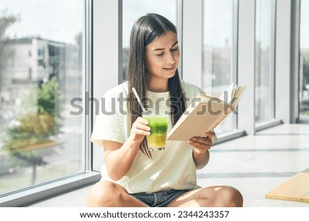 A young woman is reading a book and drinking a cooling drink.