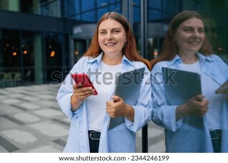 Young happy business woman wearing shirt using laptop while standing in modern workspace. High quality photo