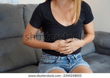 Digestive problems from poor diet. Young woman suffering from strong abdominal pain while sitting on sofa at home. Royalty-Free Stock Photo #2344248055
