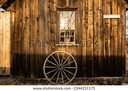 An old wooden wheel by the wooden cottage wall during autumn foliage in New England countryside, America