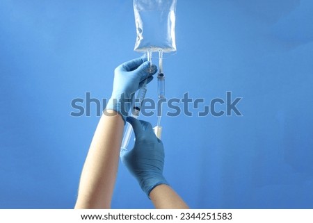Drug bag with a infusion set connected to delivery the drug to the pacient. Professional holding the bag to infuse the drug with a syringe  Royalty-Free Stock Photo #2344251583