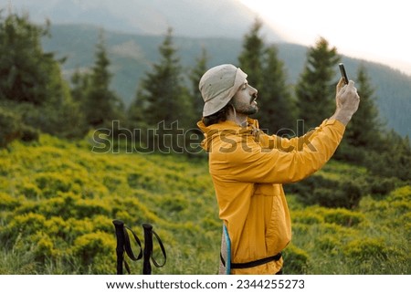 A stylish tourist with a mustache takes a photo on the phone against the background of evening mountain scenery