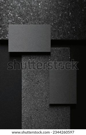 Two dark grey business cards laying flat on a dark grey concrete stone surface, Modern clean minimalism  template for luxury stationery mockup.