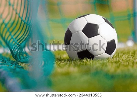 Classic football (soccer) ball on green grass ground at the back of the goal net
