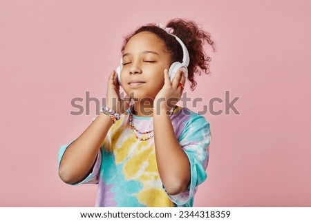 Pretty girl listening to healing or relaxation music in headphones while standing in front of camera and posing during photo session Royalty-Free Stock Photo #2344318359