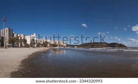 City of Santos, Brazil. Ponta da Praia beach. Buildings by the sea, strip of sand, sea, port channel and in the background the Fortaleza da Barra. Blue sky clouds.