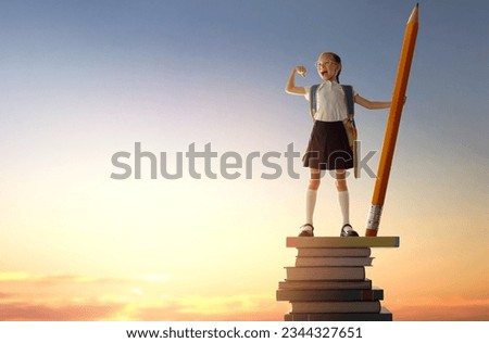 Back to school! Happy cute industrious child standing on the tower of books and holding a huge pencil on background of sunset sky. Concept of education and reading. The development of the imagination.