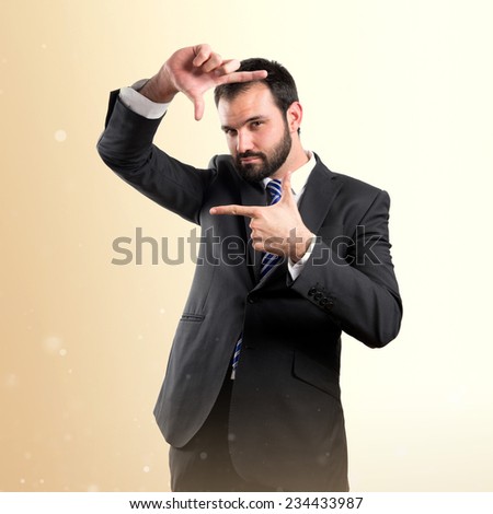 Young businessman doing a frame sign over ocher background