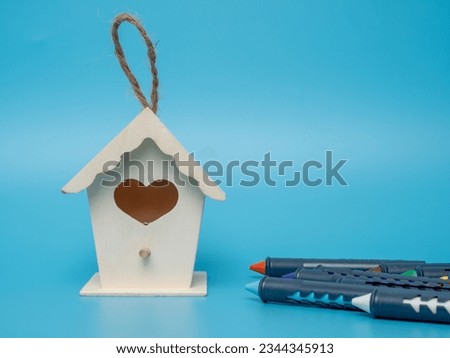 Birdhouse and multi-colored crayons for drawing on a blue background. Crayons and birdhouse close-up.