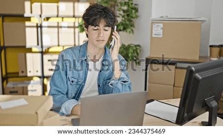 Young hispanic man ecommerce business worker talking on smartphone using laptop at office