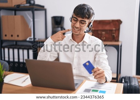 Young hispanic man working using computer laptop holding credit card smiling cheerful showing and pointing with fingers teeth and mouth. dental health concept. 