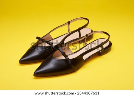 Feminine open-back black women's shoes with pointed toes isolated on a bright yellow background. Close-up view. Mock-up for design advertising for a shoe store