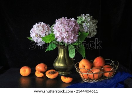 Fresh apricots in metal basket on table with flowers in bronze vases against dark background - dark and moody photography