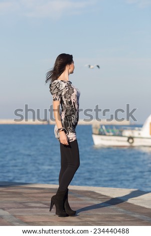 Attractive woman in black leggings on seafront. Cute business woman observes white boat in sea