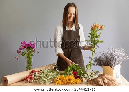 Skilled floral employee. Delicate bloom arrangements. Smiling woman florist creating beautiful bouquet at workplace in flower shop standing isolated over gray background. Professional florist workshop