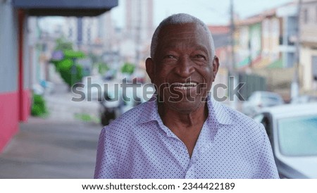 Portrait of a happy black senior Brazilian man standing in street sidewalk looking at camera with smiling expression. Elderly African American male with joyful emotio nin urban setting Royalty-Free Stock Photo #2344422189