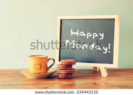 blackboard with the phrase happy monday next to cup of coffee and cookies
