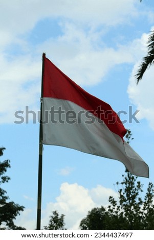 The red and white flag, the flag of the Republic of Indonesia flutters in the gentle breeze during the day.