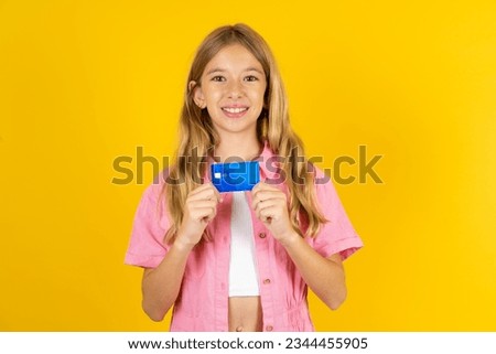 Photo of Caucasian kid girl wearing pink dress over yellow background positive smile hold credit card income salary