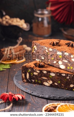 Round Italian traditional Christmas sweet Panforte with cocoa, pistachios and candied fruits on a dark wooden background. Christmas sweets of the peoples of the world