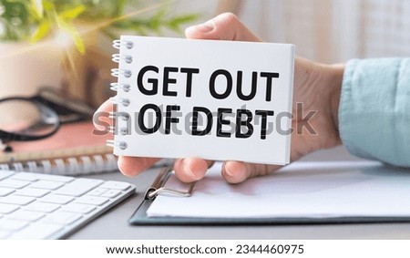 A woman is holding an open notepad with text Get Out Of Debt, against the backdrop of an office background. Royalty-Free Stock Photo #2344460975