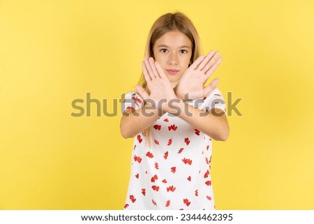 Caucasian kid girl wearing polka dot shirt over yellow background has rejection expression crossing arms and palms doing negative sign, angry face.