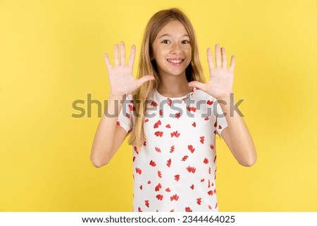 Caucasian kid girl wearing polka dot shirt over yellow background showing and pointing up with fingers number ten while smiling confident and happy.