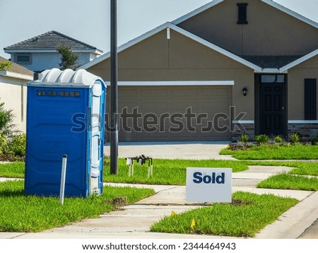 Rectangular "Sold" sign near sidewalks and a portable toilet by driveway to single-family house under construction (off-camera) in a suburban residential development in southwest Florida