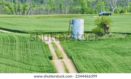 Abandoned oil pump jack next to tank with maintenance road in middle of farm field aerial