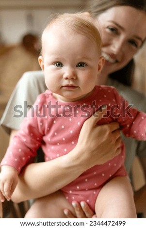 Cute nanny takes care of adorable child in kindergarten, holding her, smiling. Selective focus on baby. Toddler care concept  Royalty-Free Stock Photo #2344472499