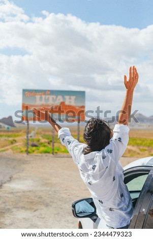 Beautiful woman on her trip by the car on the background of Welcome to Utah state border sign right in the Monument Valley. Welcome to Utah road sign.