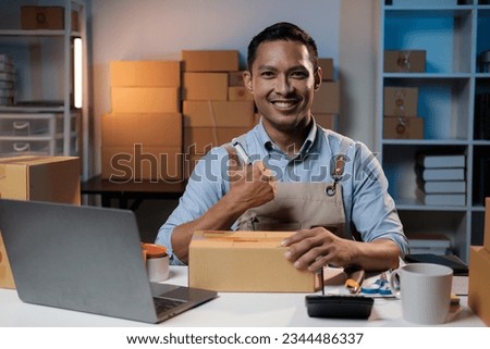 Asian small business owner showing the thumbs up sign to the camera while working in his workplace at night.