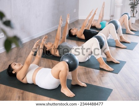 Young girl is doing Pilates in the studio. People lie on their backs holding a soft ball pilates in their outstretched legs