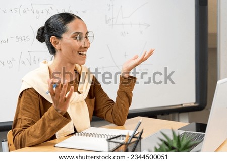 Female young Arab school math teacher, college tutor coach looking at webcam and talking in classroom giving virtual teaching remote class online lesson by zoom conference call on laptop computer. Royalty-Free Stock Photo #2344500051