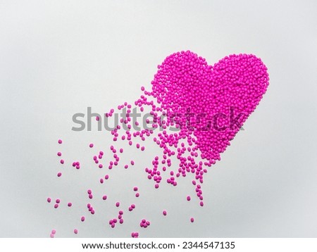 A collection of pink masterbatch granules forming a broken heart sign on a white background, this material is a coloring agent for products in the plastics industry