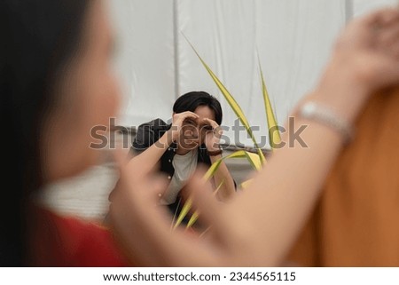 A creepy guy obsessively stalks a couple while hiding by the landscaping. An asian man obsessed over a woman who is in a relationship. Royalty-Free Stock Photo #2344565115