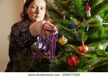 We decorate the Christmas tree. Hands hang a lilac garland of small balls on a green spruce branch close-up.

