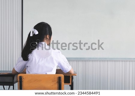 Schoolgirl sitting in classroom with white board. Asian female student in white school uniform sitting on wooden chair in classroom.students sitting in class. Student back to school.